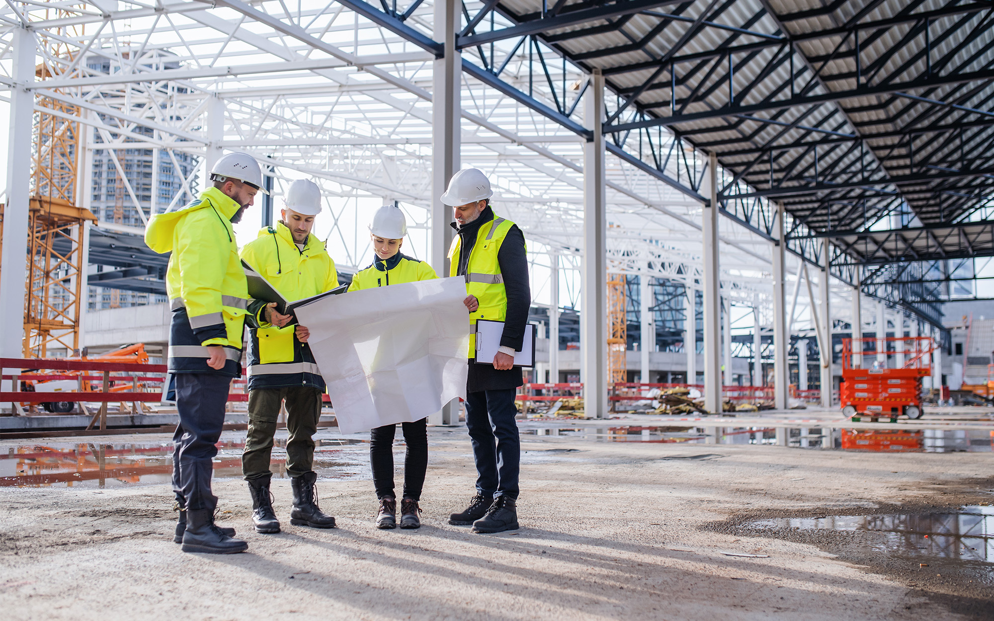 Group Of Engineers With Blueprints Standing On Construction Site