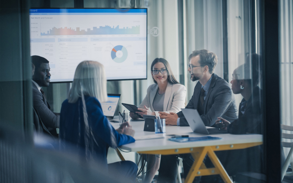 Finance Team Meets In A Glass Conference Room To Review Dashboards
